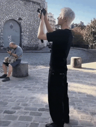 a man in a black shirt is taking a picture of another man sitting on a stone block