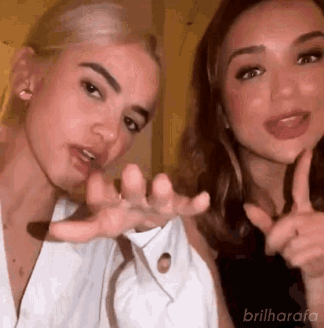 two women are standing next to each other and making a peace sign with their hands .