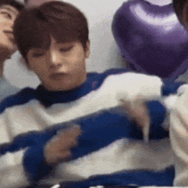 a man in a blue and white striped sweater is sitting in front of purple balloons .