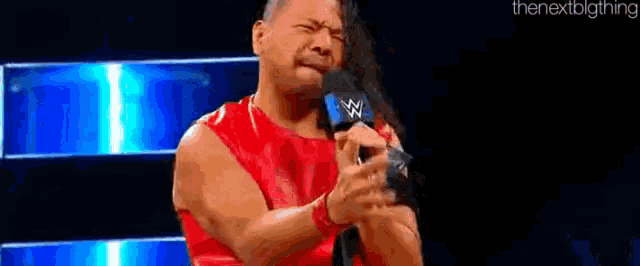 a man in a red shirt is holding a microphone and making a face .