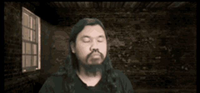 a man with long hair and a beard is standing in front of a window