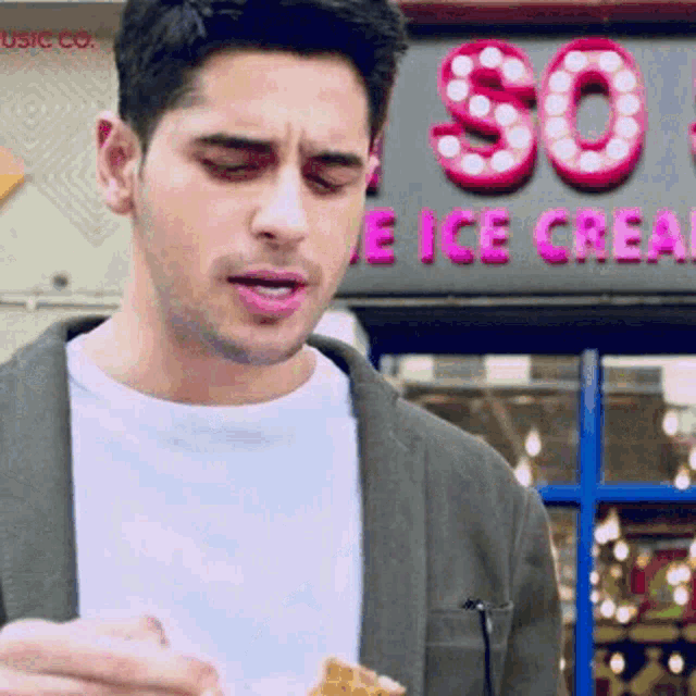 a man is eating an ice cream cone in front of a store called so ice cream