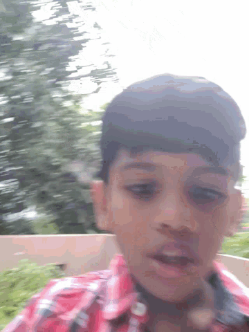 a boy in a red and black plaid shirt looks at the camera
