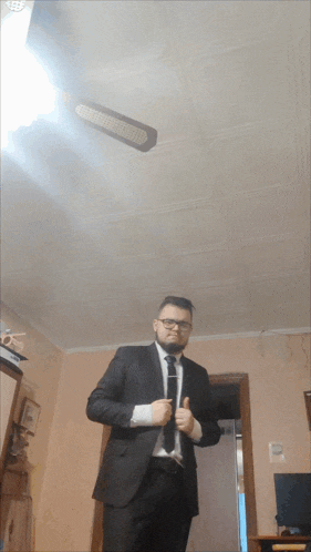 a man in a suit and tie giving a thumbs up in front of a ceiling fan