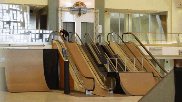 a red bull sign hangs above an escalator in a mall