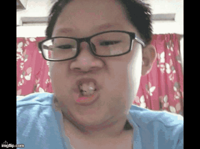 a young boy wearing glasses and a blue shirt making a funny face