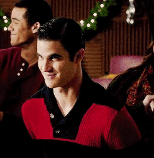a man in a red and black sweater is smiling while standing next to two other men .