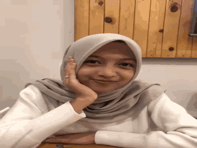 a woman wearing a hijab and a white sweater is smiling for the camera