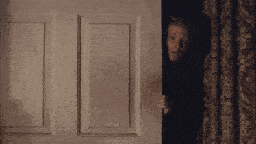 a woman is peeking out of a doorway .