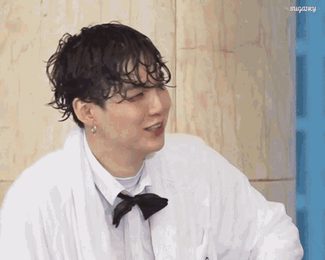 a man wearing a white robe and a black bow tie has the word sugary on the bottom right