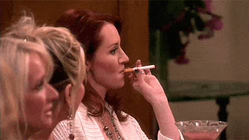 a woman is smoking a cigarette while another woman holds a drink