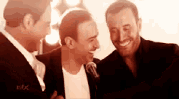 a group of three men are standing next to each other and laughing .