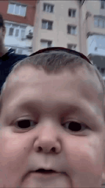 a close up of a baby 's face with a building in the background