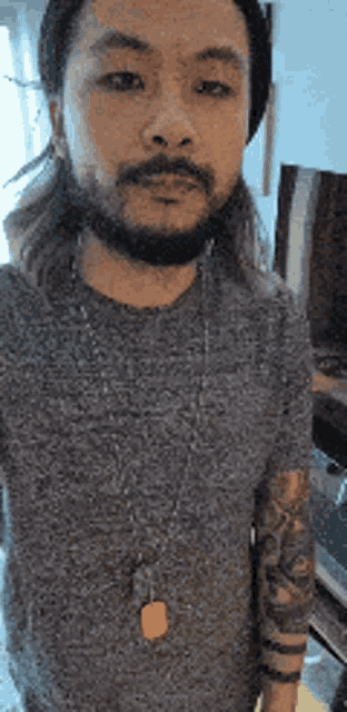 a man with a beard and long hair is wearing a gray shirt and a hat .