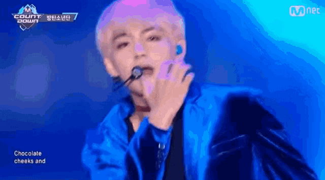 a man in a blue jacket is singing into a microphone while wearing a choker .