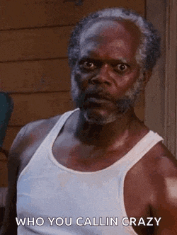 a man with a beard wearing a white tank top is standing in front of a building .