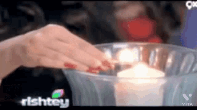 a woman 's hand is reaching into a glass bowl with a candle in it .