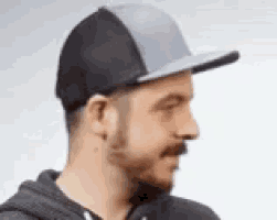 a man with a beard and mustache is wearing a black and grey baseball cap .
