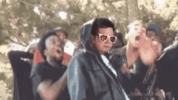 a man wearing sunglasses and a hoodie is standing in a crowd of people .