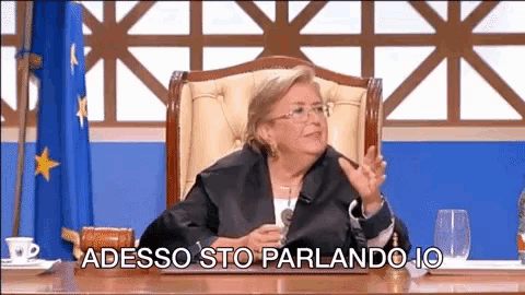 a woman is sitting at a desk with the words " adesso sto parlando io " written below her