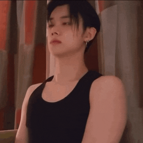 a young man wearing a black tank top is sitting in front of a window .