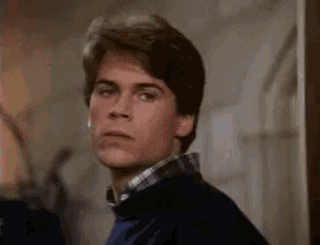 a young man in a blue sweater and plaid shirt is standing in a room .