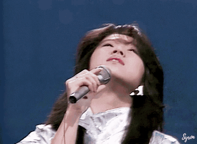 a woman singing into a microphone with her eyes closed
