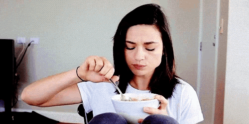 a woman is sitting on a chair eating cereal with a spoon .
