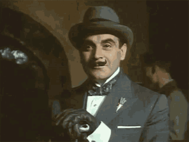 a man in a tuxedo and hat is holding his gloves