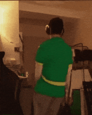 a man wearing headphones and a green shirt is walking in a room