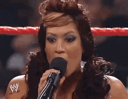 a woman is holding a microphone in her hand in a wrestling ring .