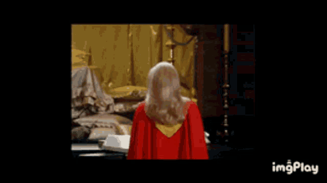 a woman in a red cape is standing in a room with a black background .