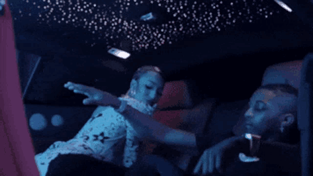a man and a woman are sitting in the back seat of a car with a starry ceiling