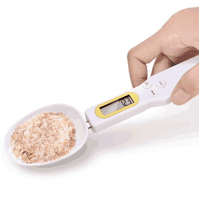 a person is measuring a spoon with a digital scale that says 12.3
