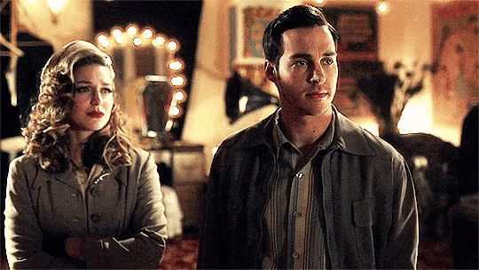 a man and a woman are standing next to each other in a room with a mirror in the background .