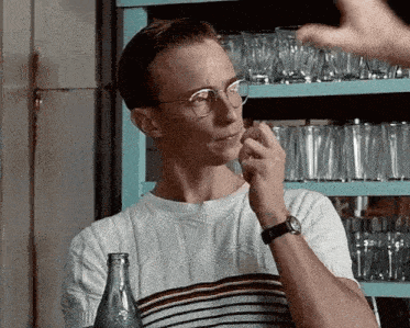 a man wearing glasses and a watch is standing in front of a shelf full of glasses .