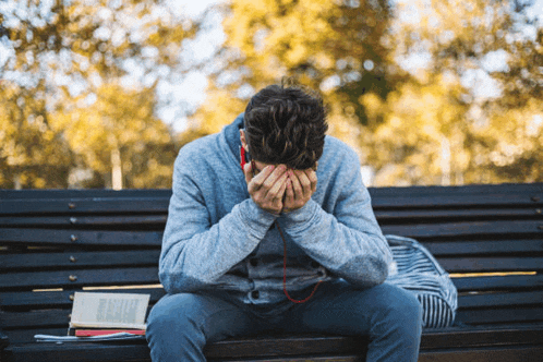 a young man sits on a bench with his head in his hands