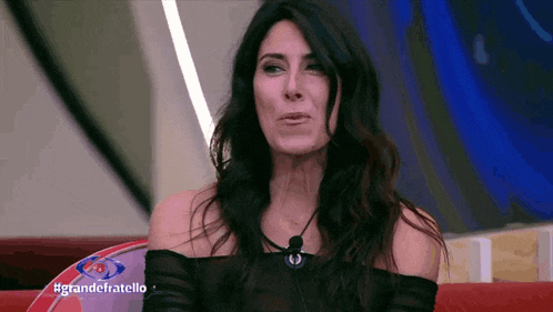 a woman with long dark hair is sitting on a red couch with the words grandefratello written on the bottom