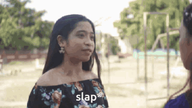 a woman in a floral off the shoulder top is talking to another woman in a park .