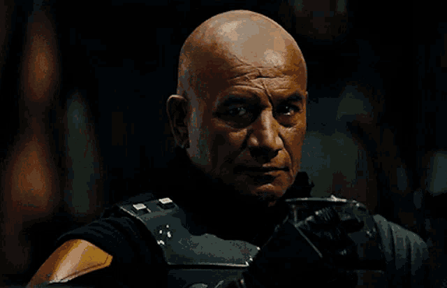 a bald man is wearing a helmet and gloves and looking at the camera
