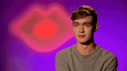 a young man is sitting in front of a purple background with a red heart in the background .