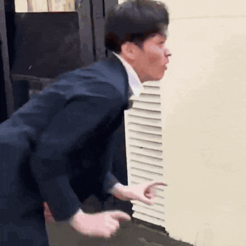 a man in a suit and tie is standing next to a wall and making a funny face .