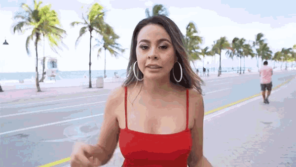 a woman in a red top and hoop earrings is walking down a sidewalk