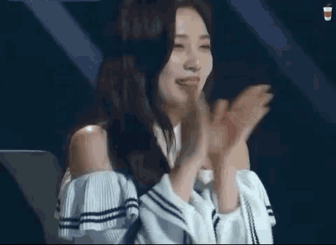 a young woman is smiling and clapping her hands while wearing a white off the shoulder sweater .