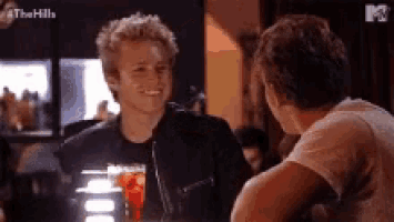 two men are sitting at a bar talking to each other and one of them is smiling .