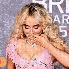 a woman in a pink dress is covering her mouth with her hands .
