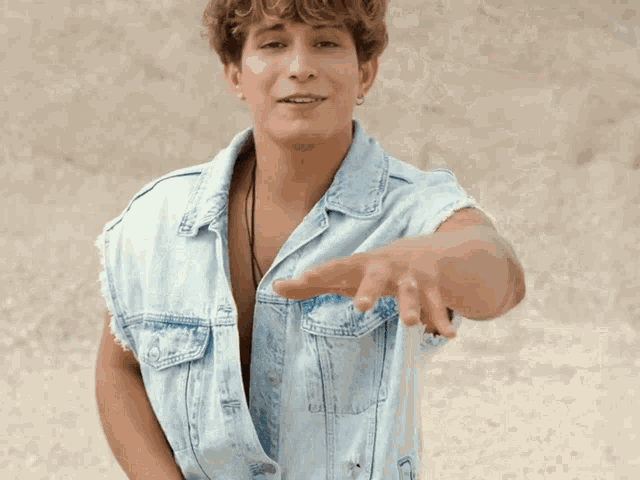 a young man wearing a denim vest without a shirt is smiling