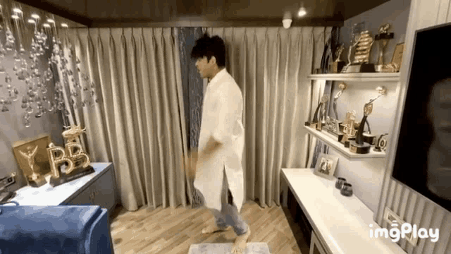 a man in a white shirt is dancing in a living room with awards on shelves and a gif that says imgplay