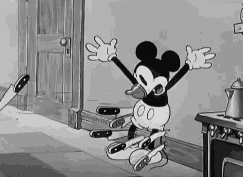 a black and white cartoon of mickey mouse sitting on the floor with his arms outstretched in a kitchen .