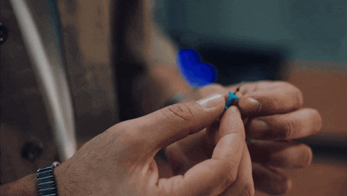 a close up of a person 's hands holding a small blue object
